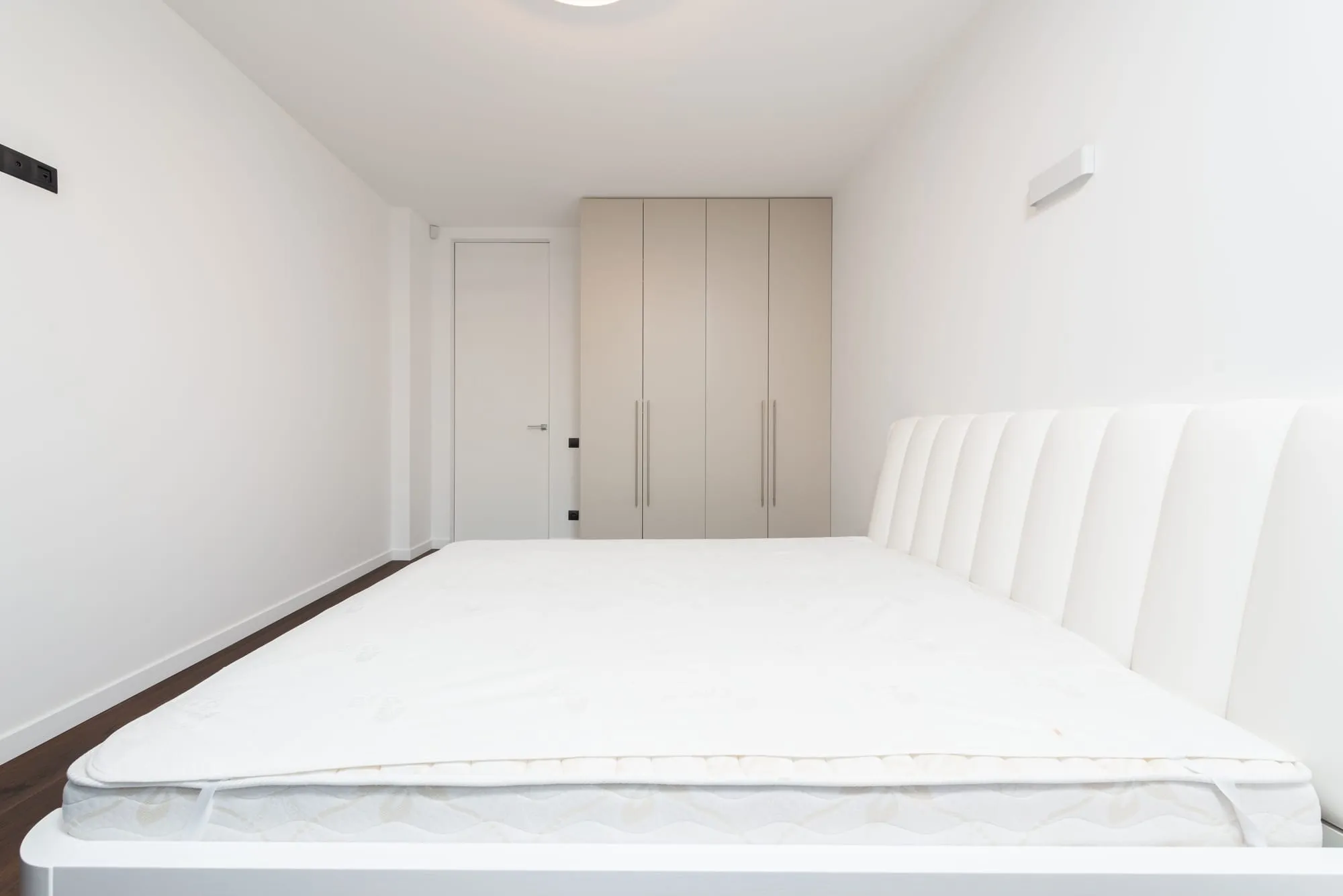Wit matras op een wit bedframe in een lichte, rustige slaapkamer