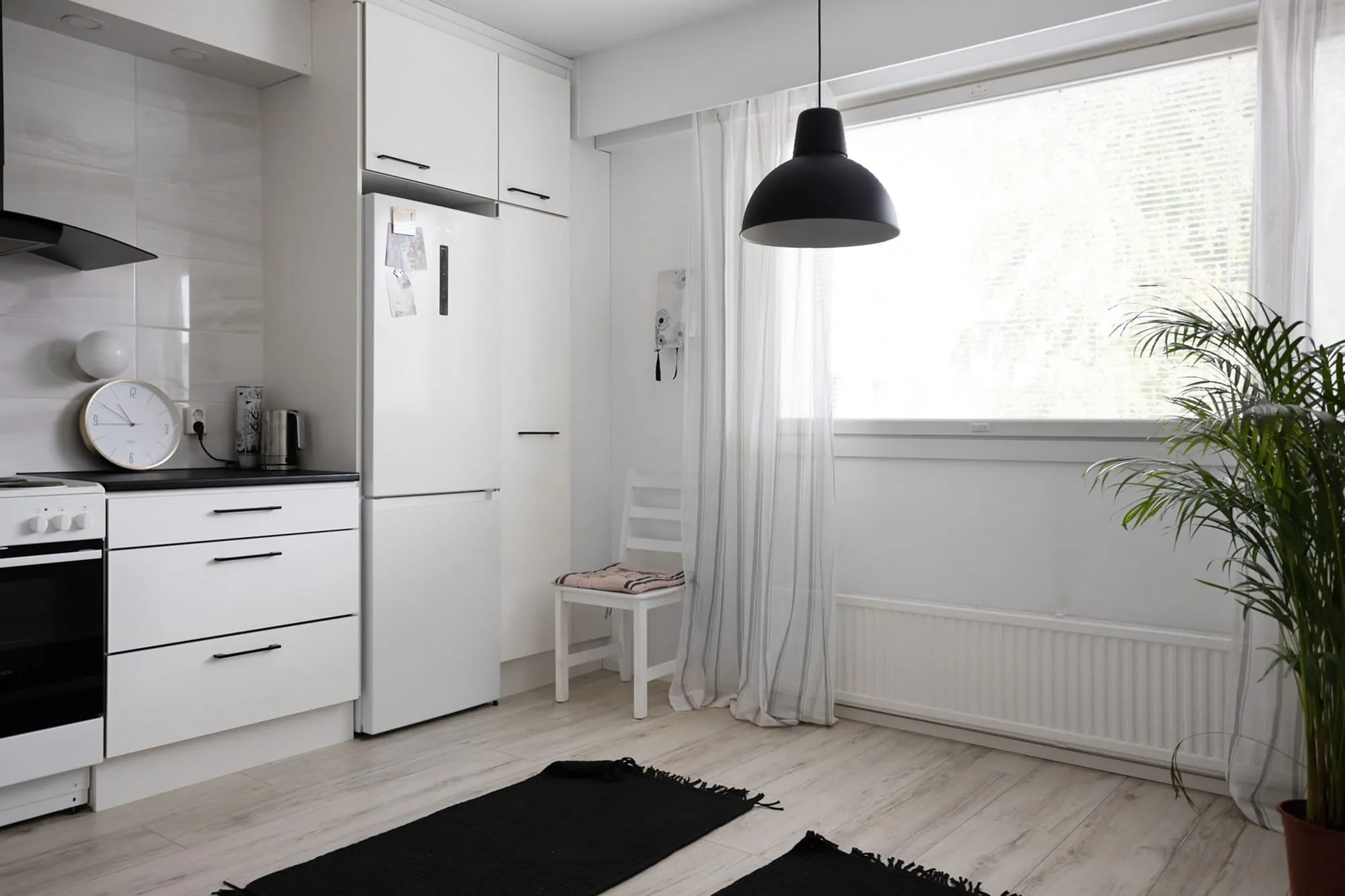 Lichte, schone keuken met witte kasten, een zwarte hanglamp en een groot raam