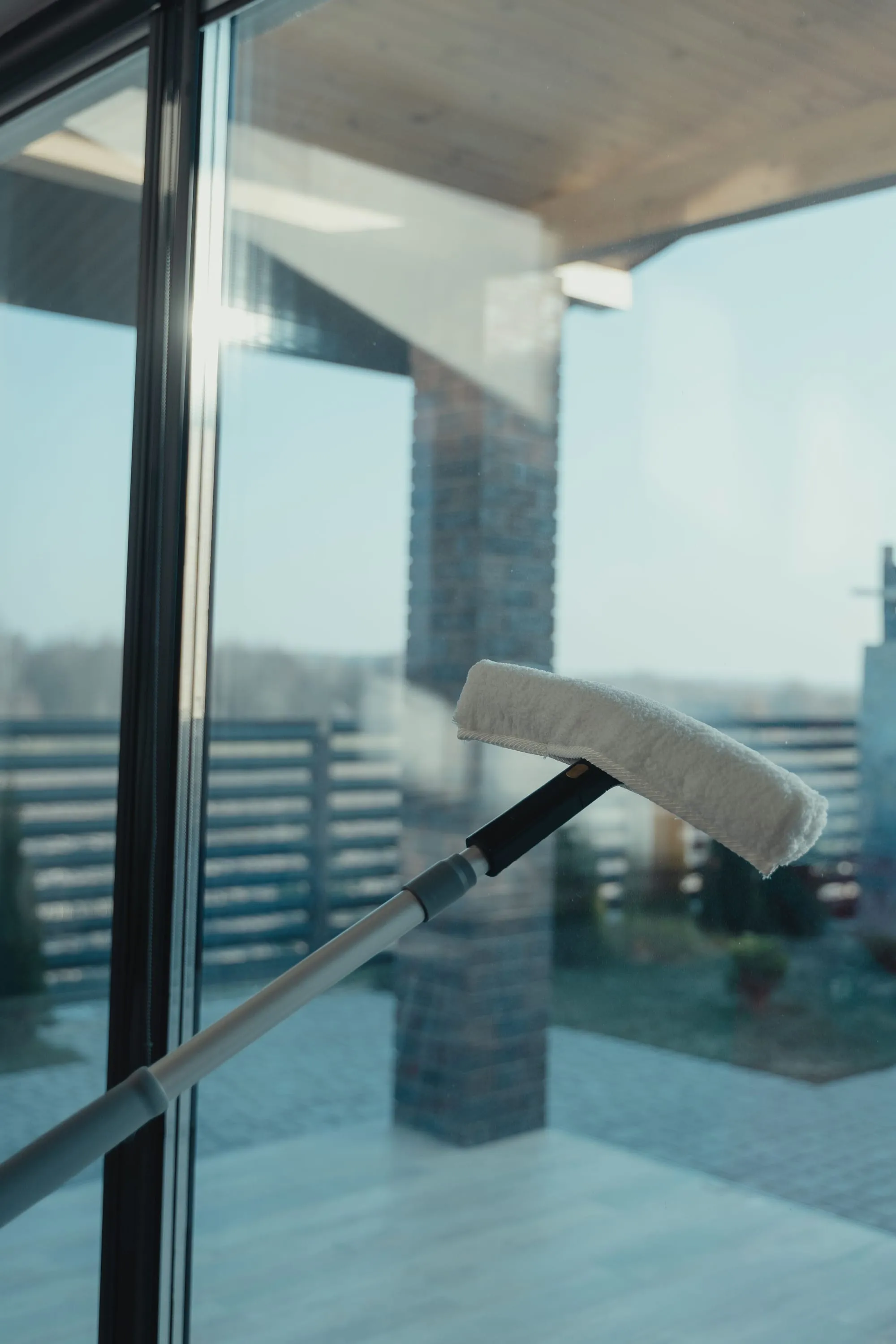 Telescopische ramenwisser met microvezelkop op een groot glazen schuifraam met uitzicht op een terras