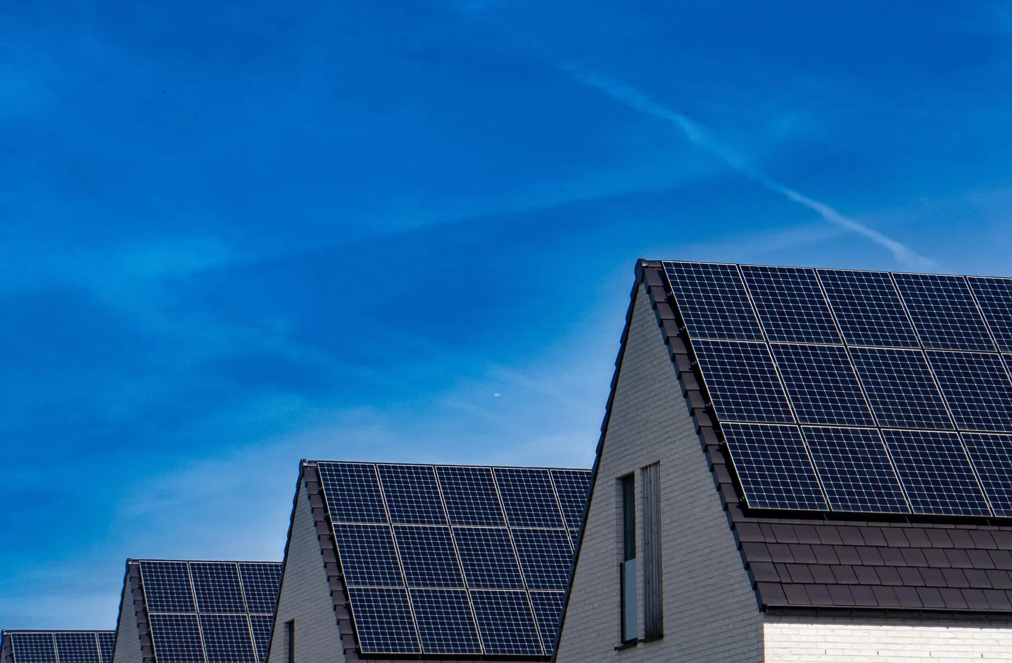 Zonnepanelen op de daken van moderne woningen met witte gevels onder een blauwe lucht